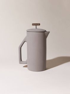 a gray coffee pot with a wooden handle on the side and a white wall behind it