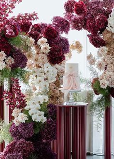 a wedding cake on top of a table surrounded by purple and white flowers in front of a window