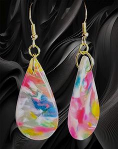 a pair of colorful earrings hanging from gold hooks on a black background with swirls