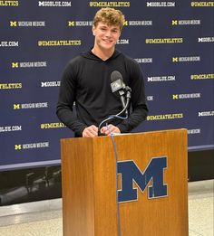 a young man standing at a podium with a microphone in front of him and smiling