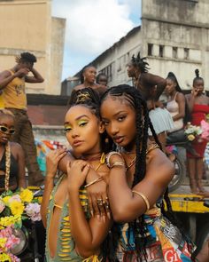 two women standing next to each other in front of a group of people on the street