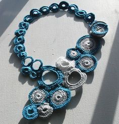 a blue and white crocheted necklace with circles on the clasp, attached to a chain