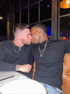 two men sitting at a table kissing each other