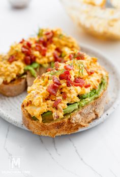 two pieces of toast with scrambled eggs and vegetables on them sitting on a white plate