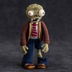 a crocheted zombie wearing a red tie and brown jacket with his hands in his pockets