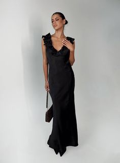 a woman in a long black dress holding a purse and looking off to the side