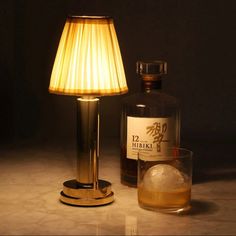 a bottle of liquor next to a glass with ice in it and a lamp on the table