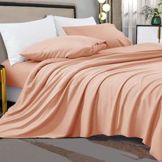 an unmade bed with peach colored sheets and pillows