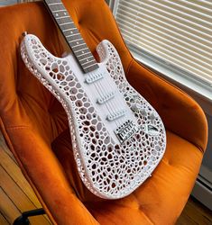 an electric guitar sitting on top of a orange chair in front of a window with blinds