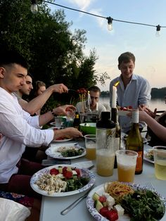 a group of people sitting around a table with plates of food and drinks in front of them