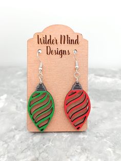 a pair of red, green and black earrings sitting on top of a wooden plaque