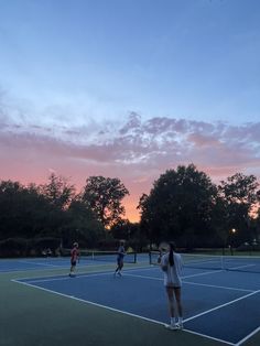 several people are playing tennis on a court at sunset or dawn with trees in the background