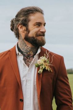 a man with a beard wearing a red suit and flower in his lapel collar