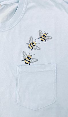 two bees embroidered on the back of a light blue t - shirt with a pocket