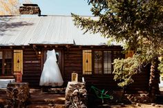 a wedding dress hanging on a clothes line in front of a log cabin with a bicycle