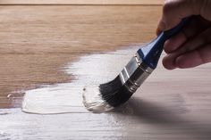 a person is holding a paint brush and painting the floor with white paint on it