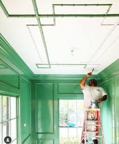 a man on a ladder painting the ceiling in a room with green walls and white trim