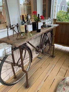 an old bicycle is sitting on the porch with wine bottles and glasses in front of it