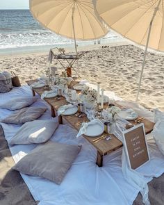 a table set up on the beach with an umbrella over it for people to eat