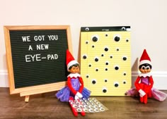 two elf dolls sitting next to a board with eye - pad on it