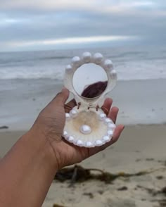 a hand holding an object in front of the ocean on a beach with waves coming in