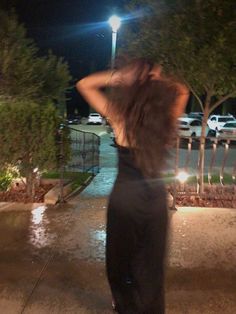 a woman in a black dress walking down the street at night with her back to the camera