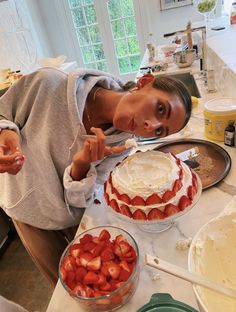 a woman holding a knife over a cake with strawberries on the table next to it