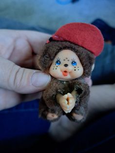 a person holding a small teddy bear with blue eyes and a red hat on it's head