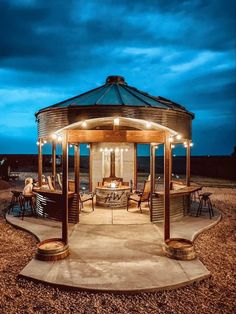 a wooden gazebo with lights on it in the middle of a gravel field at night