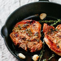 two pork chops in a skillet with garlic and herbs