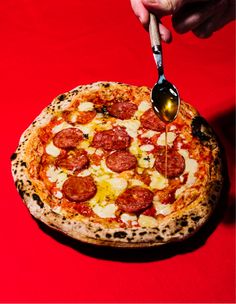 a pepperoni and cheese pizza being drizzled with a spoon on a red surface