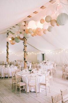 the inside of a tent with tables and chairs set up for a wedding reception under paper lanterns