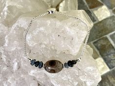 This 1.8 mm Sterling Silver Petoskey stone bracelet features a lovely Oval Petoskey stone surrounded by Leland blue chip beads and sterling silver beads. The bracelet chain is fully adjustable to a maximum of 8.5 inches using a move able coin-shaped silicone lined bead that slides along the chain. This chain is plated with fine silver to ensure a bright white color and protect against tarnish. Petoskey stones aren't real stone but rather a fossilized coral only found in the northern portions of Adjustable Sterling Silver Bracelet With Natural Stones, Adjustable Oval Sterling Silver Bracelet Nickel Free, Adjustable Oval Bracelet With Natural Stones, Adjustable Sterling Silver Beaded Bracelets With Stones, Adjustable Oval Sterling Silver Bracelets, Adjustable Oval Spiritual Bracelets, Adjustable Oval Bracelets, Adjustable Oval Bracelets For Everyday, Adjustable Oval Bracelet With Stones