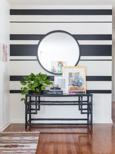 a black and white striped wall with a round mirror on the end table in front of it