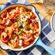 a skillet filled with pasta and shrimp on top of a blue checkered table cloth