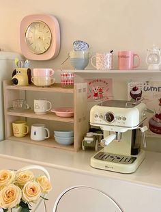 there is a coffee maker on the counter next to some plates and flowers in a vase