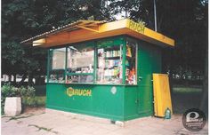 a small green and yellow kiosk sitting on the side of a road next to trees