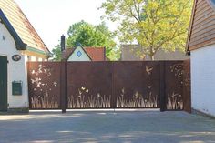 an iron fence in front of a house with tall grass growing on the side and trees behind it