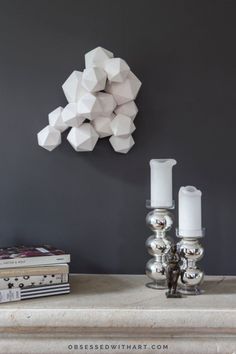 two candles are sitting on a table next to some books and a wall sculpture in the background