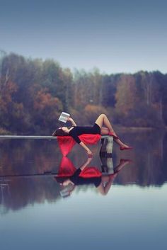 a woman is laying on the edge of a body of water with trees in the background