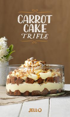 carrot cake trifle in a glass dish sitting on a table next to a vase with flowers