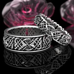 two wedding rings sitting next to each other on top of a black surface with pink glass in the background