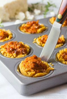 someone using a knife to cut into cupcakes in a muffin tin with sauce on top