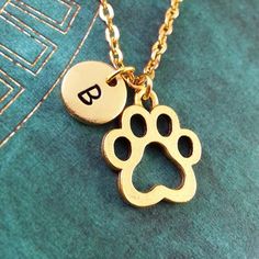 a dog's paw and initial charm on a green shirt with a gold chain