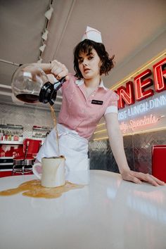 a woman pouring liquid into a glass on top of a table in a diner's kitchen