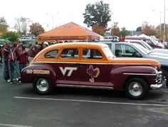 an orange and maroon car parked in a parking lot next to other cars with people standing around it