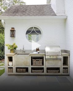 an outdoor kitchen is shown in front of a white brick building with windows and shutters