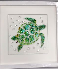 a sea turtle made out of green and white beads in a square frame on the wall