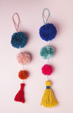 three pom - poms hanging from strings on a pink background, one is multicolored and the other has tassels