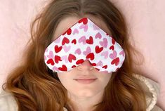 a woman with red hair wearing a white and pink heart print eye mask